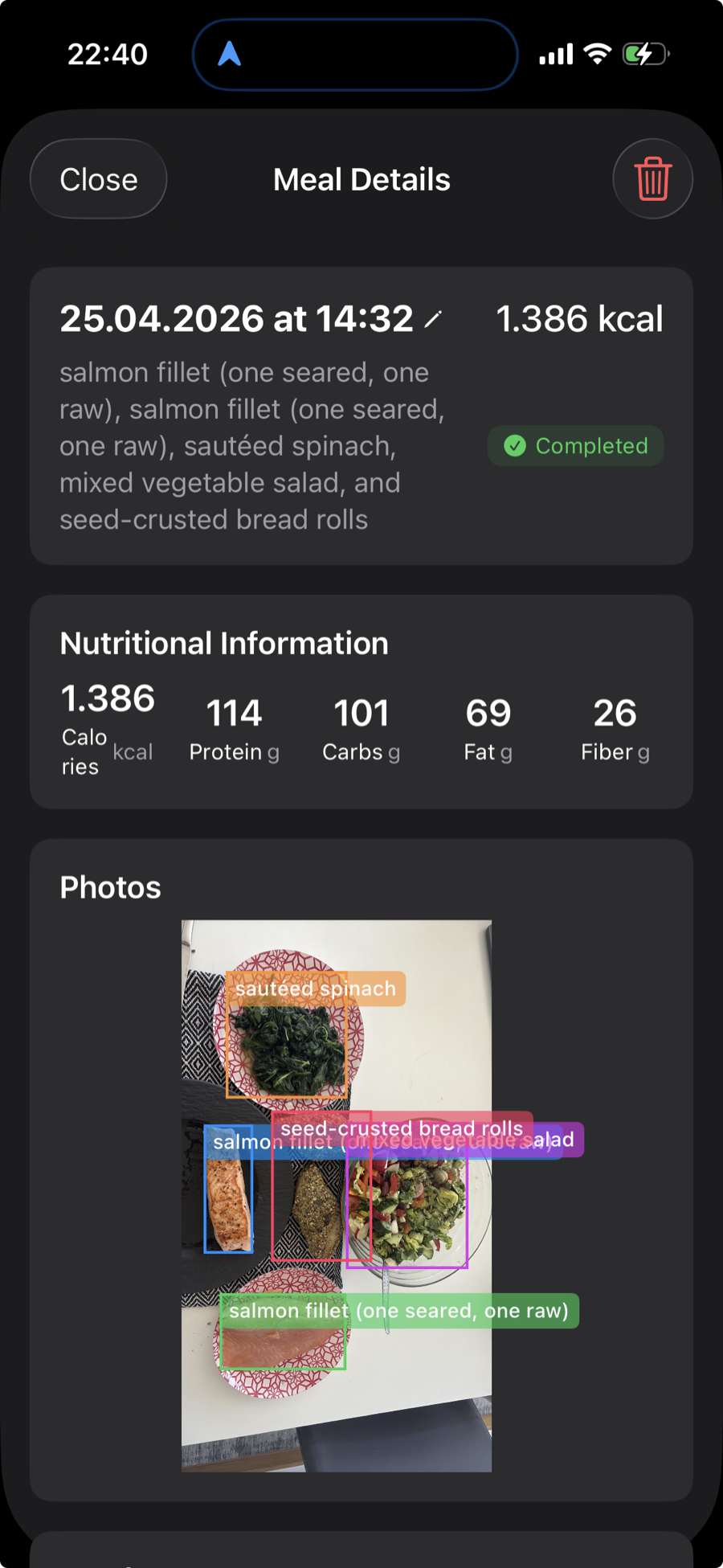 A meal photo analyzed by the app, with each food item outlined and labeled — salmon fillets, sautéed spinach, mixed vegetable salad, and seed-crusted bread rolls — alongside total calories and macros.